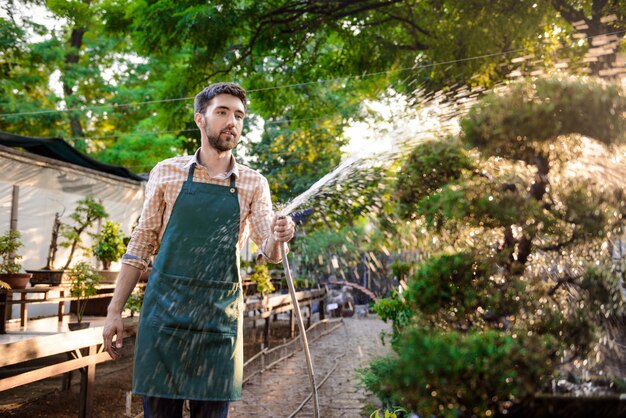 若いハンサムな陽気な庭師笑顔、水遣り、植物の世話