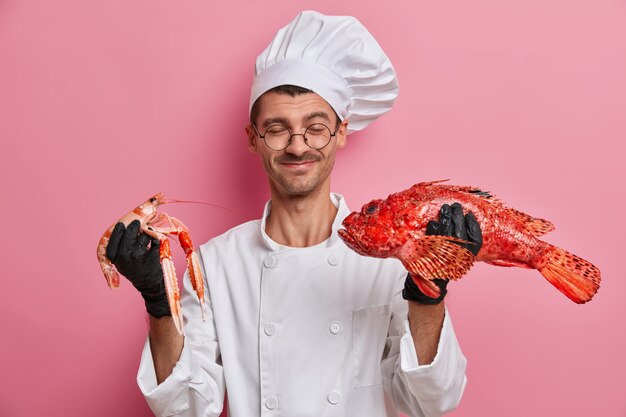 Young handsome chef holding uncooked crayfish isolated