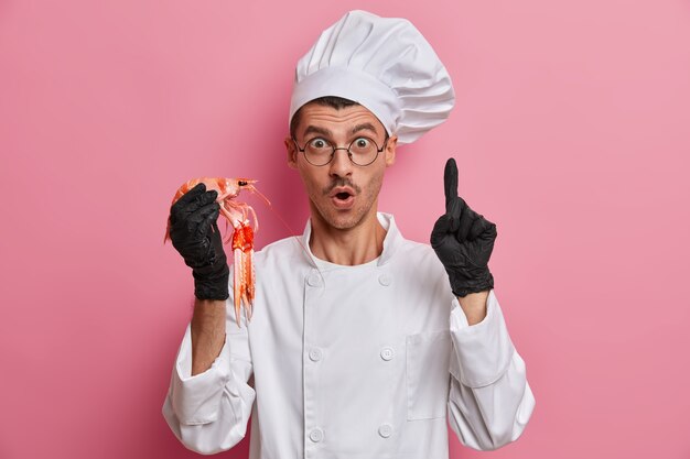 Young handsome chef holding uncooked crayfish isolated