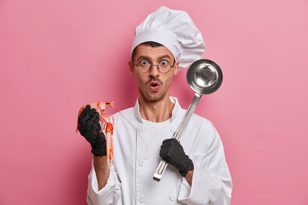 Young handsome chef holding uncooked crayfish isolated