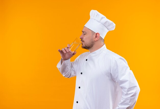 Young handsome cook in chef uniform drinking water with closed eyes isolated on orange space 