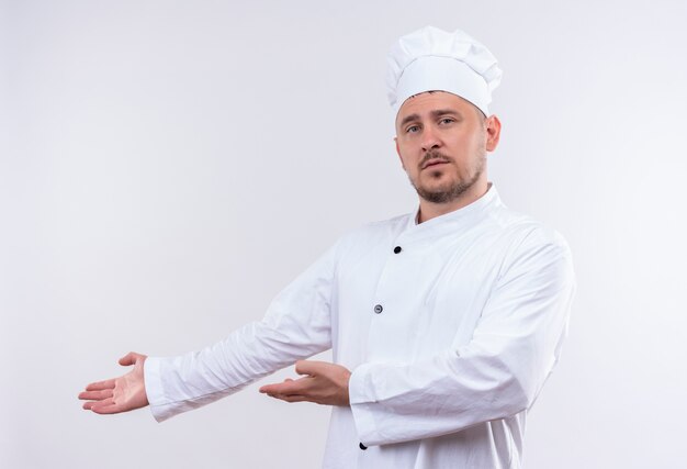 흰색 공간에 고립 된 측면에서 손으로 가리키는 요리사 유니폼에 젊은 잘 생긴 요리사