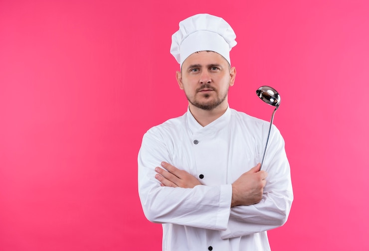 Free Photo young handsome cook in chef uniform standing behind white wall looking straight isolated on orange space 
