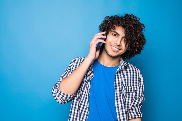 Young handsome curly man talking on the phone isolated on blue wall