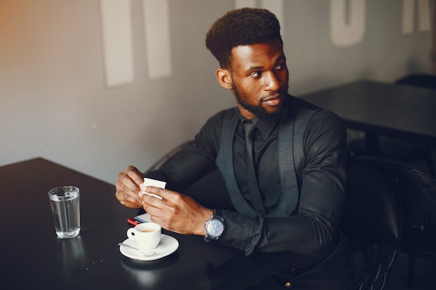 A young and handsome dark-skinned boy in a black suit sitting in a cafe