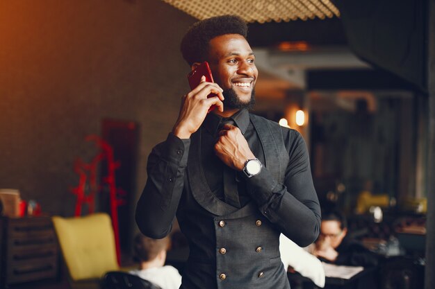 A young and handsome dark-skinned boy in a black suit sitting in a cafe