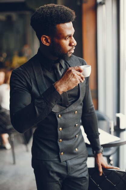 A young and handsome dark-skinned boy in a black suit standing in a cafe