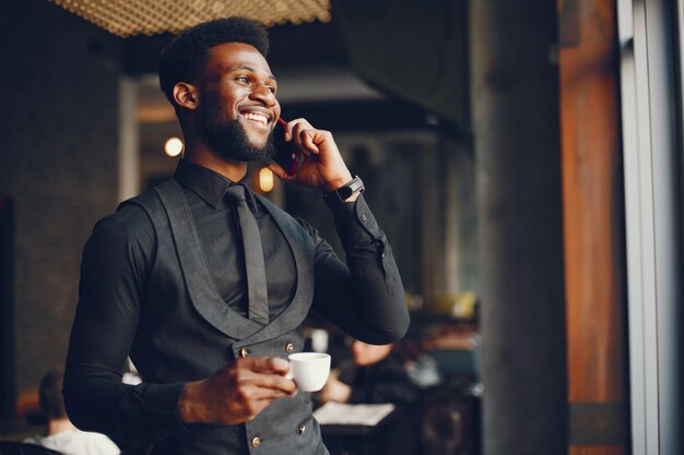 A young and handsome dark-skinned boy in a black suit standing in a cafe