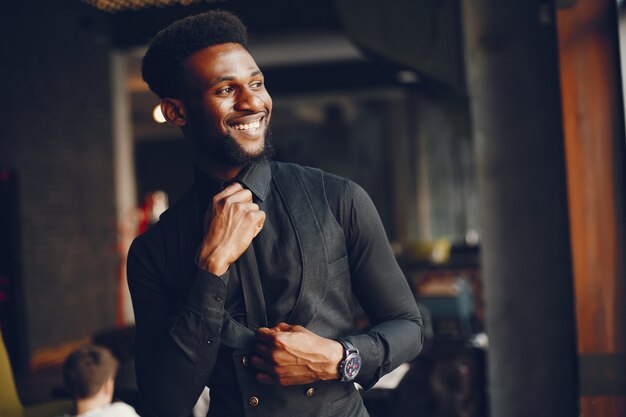 A young and handsome dark-skinned boy in a black suit standing in a cafe