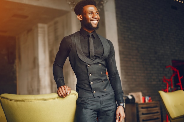 A young and handsome dark-skinned boy in a black suit standing in a cafe