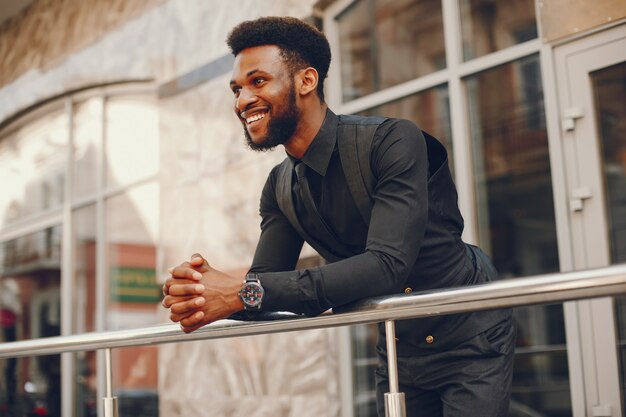 A young and handsome dark-skinned boy in a black suit standing in a city