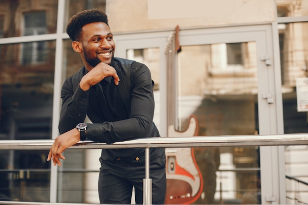 A young and handsome dark-skinned boy in a black suit standing in a city