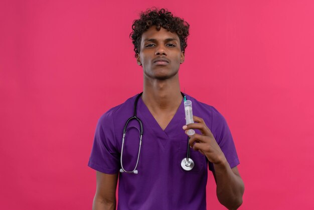 注射器を持って紫の制服を着た巻き毛の若いハンサムな浅黒い医者