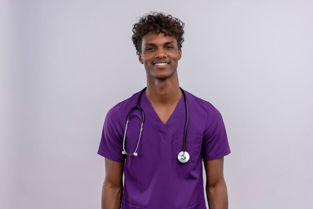 A young handsome dark-skinned doctor with curly hair wearing violet uniform with stethoscope smiling while  