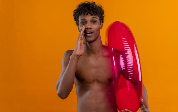 A young handsome dark-skinned man with curly hair calling someone while holding inflatable pool ring 