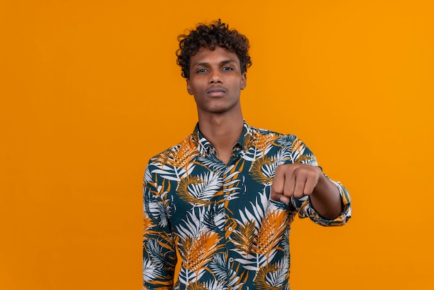 A young handsome dark-skinned man with curly hair in leaves printed shirt pointing at camera with clenched fist