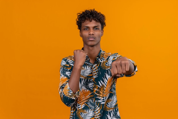 A young handsome dark-skinned man with curly hair in leaves printed shirt practicing box moves 