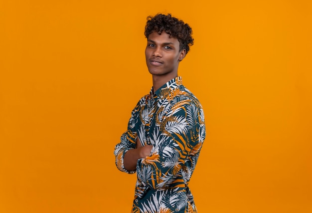 Free photo a young handsome dark-skinned man with curly hair in leaves printed shirt standing and