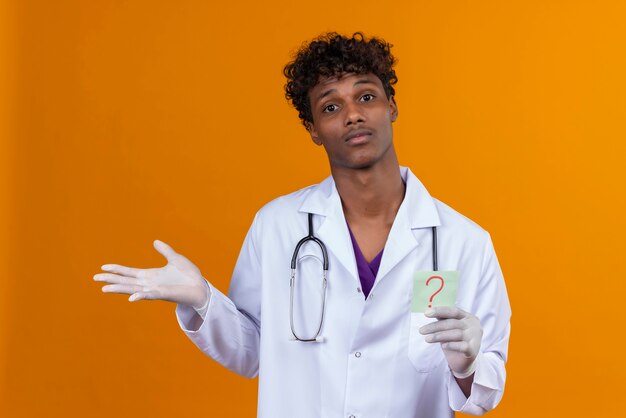 A young handsome dark-skinned man with curly hair wearing white coat with stethoscope showing a paper card with the question mark 