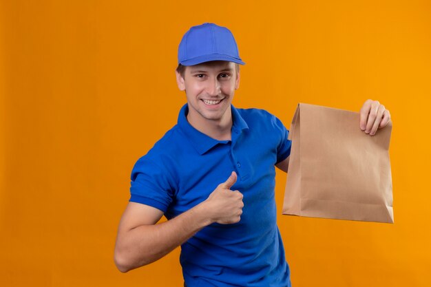 青い制服を着た若いハンサムな配達人と自信を持って探して紙packgaeを保持しているキャップ