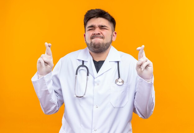 Молодой красивый врач в белом медицинском халате, белые медицинские перчатки и стетоскоп, закрывающий глаза