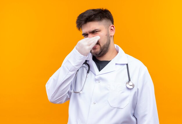 Young handsome doctor wearing white medical gown white medical gloves and stethoscope