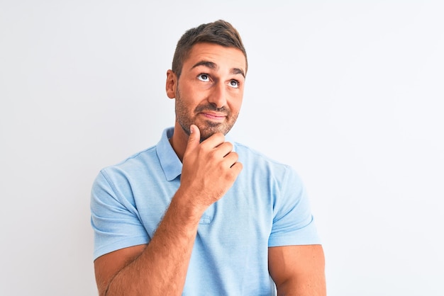 Young handsome elegant man wearing blue tshirt over isolated background with hand on chin thinking about question pensive expression Smiling with thoughtful face Doubt concept