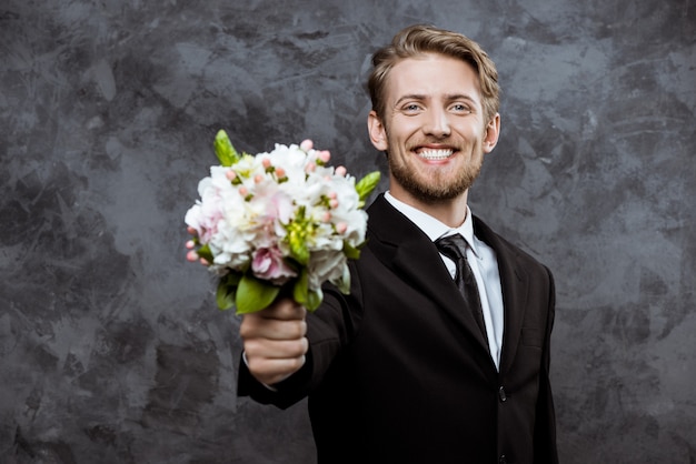 Giovane sposo bello sorridente, con bouquet da sposa