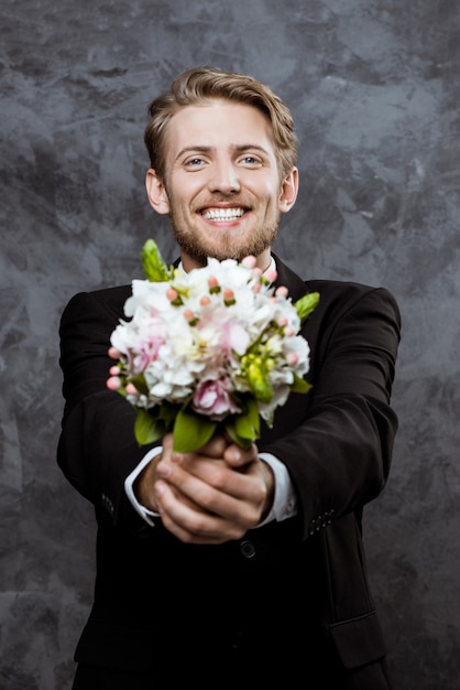 Young handsome groom smiling, holding bridal bouquet