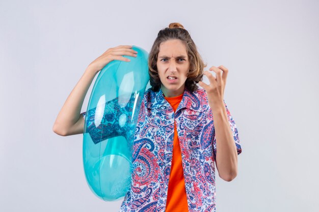 Young handsome guy holding inflatable ring mad and crazy standing with arms raised 