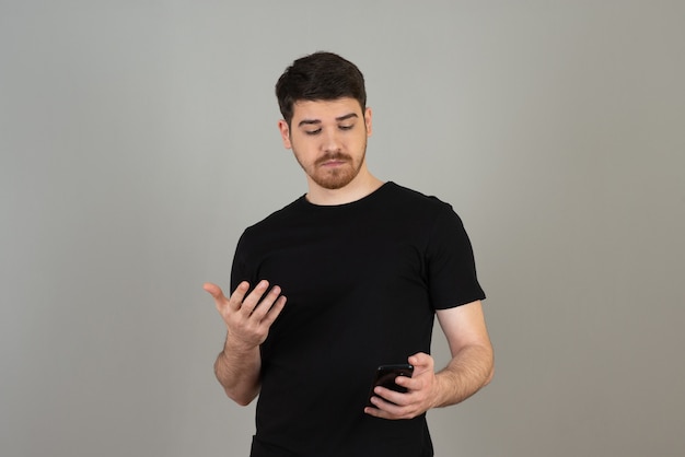 Young handsome guy looking at phone on a grey.