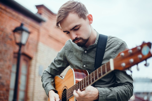 Free photo young handsome guy plays the guitar, picks up a chord, street musician