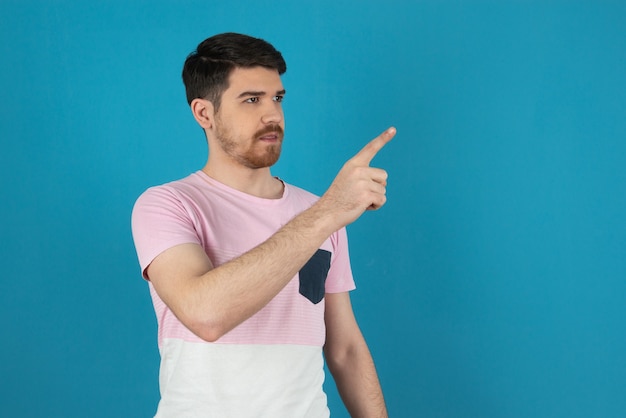 Free photo young handsome guy pointing finger to air and looking away on blue.