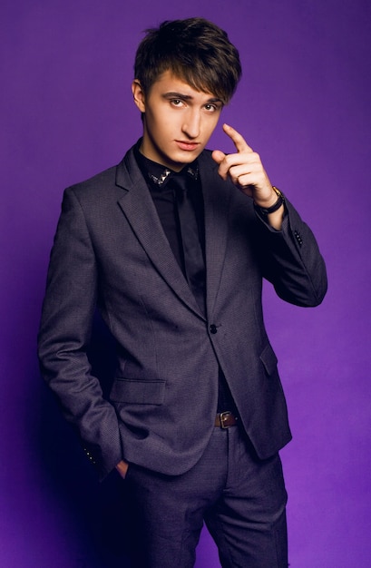 Young handsome guy posing at studio in stylish grey suit, businessman style, violet purple studio background.