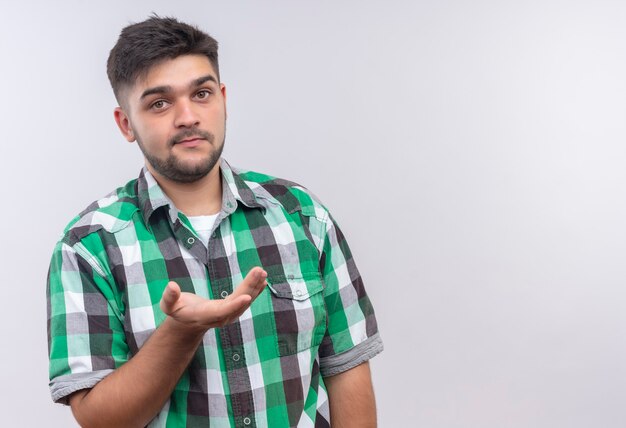 Young handsome guy wearing checkered shirt asking what's new standing over white wall