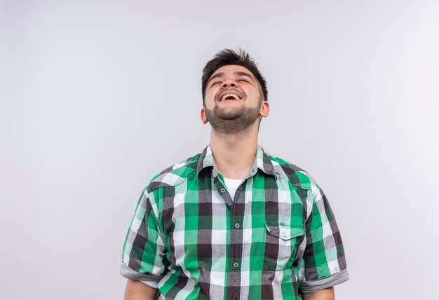 Young handsome guy wearing checkered shirt happily laughing standing over white wall