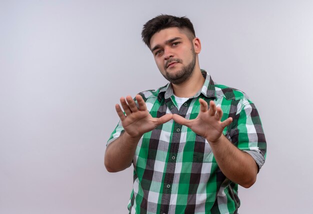 Young handsome guy wearing checkered shirt looking bewaring standing over white wall