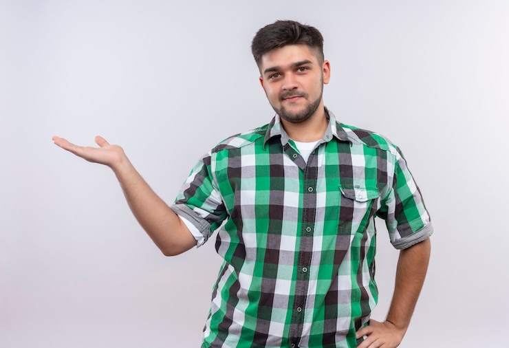 मुफ़्त फोटो young handsome guy wearing checkered shirt smiling pointing to the right with hand standing over white wall