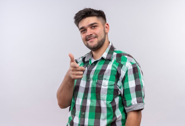 Young handsome guy wearing checkered shirt smiling pointing standing over white wall