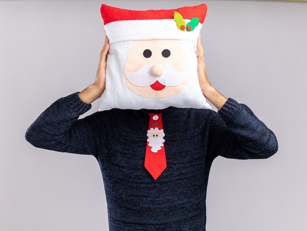 Free photo young handsome guy wearing christmas tie with hair hoop covered face with christmas pillow isolated on white background