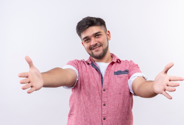 Free photo young handsome guy wearing pink polo shirt cordially greets standing over white wall