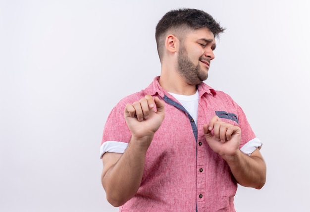 Young handsome guy wearing pink polo shirt disdained looking besides standing over white wall