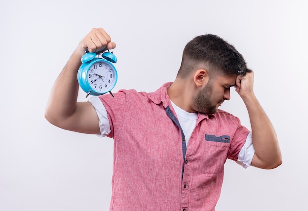 Free photo young handsome guy wearing pink polo shirt looking besides upset for being late holding his head with fist standing over white wall