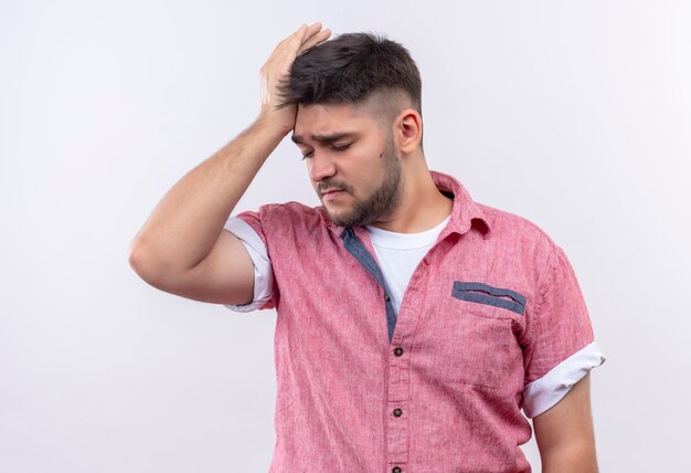 Young handsome guy wearing pink polo shirt suffering from headache holding his head with hand standing over white wall