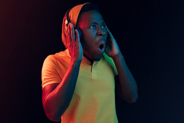 Молодой красивый счастливый хипстерский мужчина слушает музыку в наушниках в черной студии