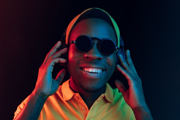 Free photo the young handsome happy hipster man listening music with headphones at black  with neon lights