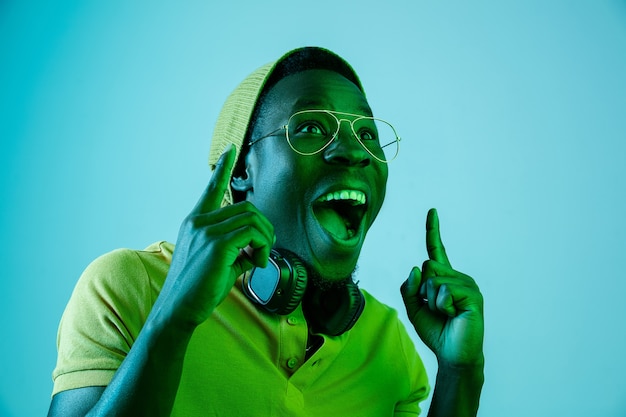 The young handsome happy surprised hipster man listening music with headphones at studio with neon lights. Disco, night club, hip hop style, positive emotions, face expression, dancing concept