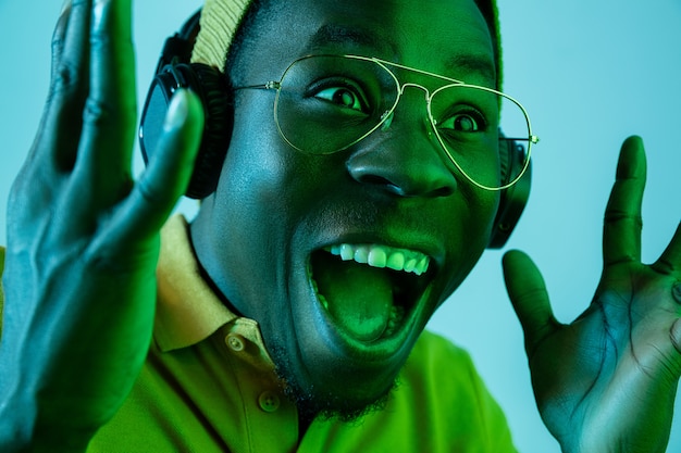 The young handsome happy surprised hipster man listening music with headphones at studio with neon lights. Disco, night club, hip hop style, positive emotions, face expression, dancing concept