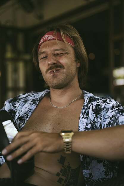 A young handsome hippie man in a red bandana with a bare torso rolls a tobacco cigarette in a cafe in Bali.