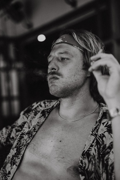 A young handsome hippie man in a red bandana with a bare torso rolls a tobacco cigarette in a cafe in Bali.